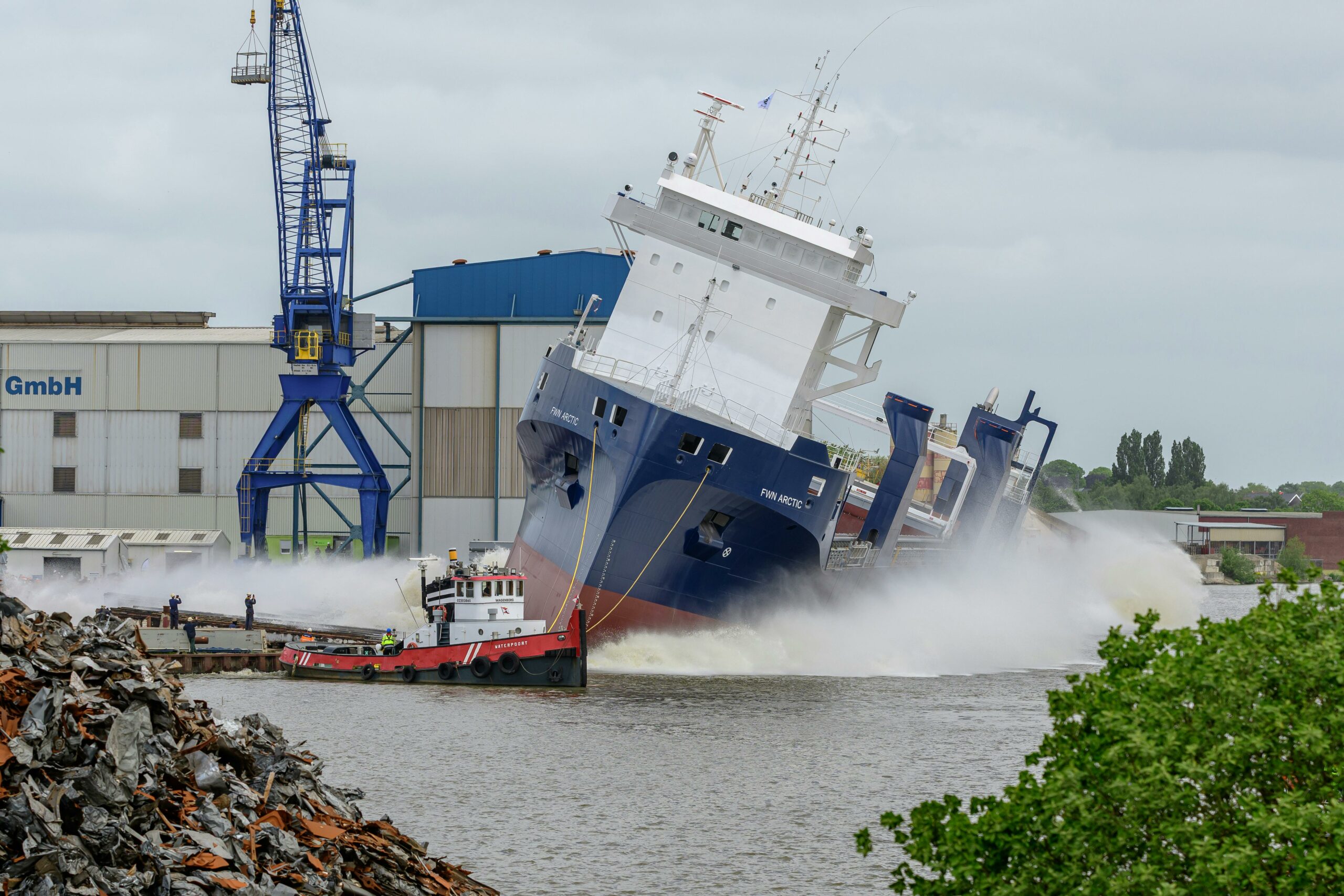 Dramatic cargo ship launch at a Niedersachsen shipyard, Germany, with industrial cranes.